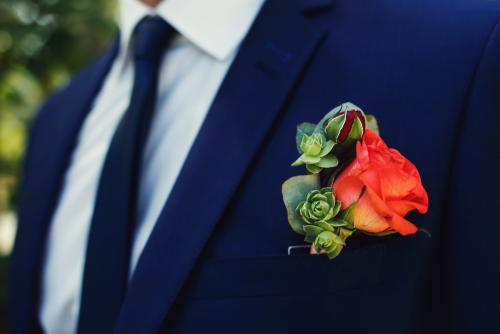 Red rose flower fresh boutonniere on stylish dark blue suit clos